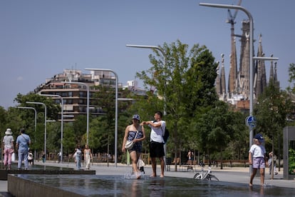 Varias personas se remojan los pies en una fuente ornamental del parque de Glòries de Barcelona durante un episodio de calor, de fondo, la Sagrada Familia.