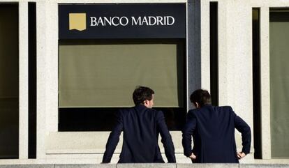 Dos hombres esperan en la puerta de la sede de Banco Madrid.