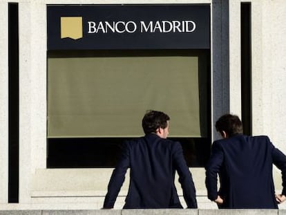 Dos hombres esperan en la puerta de la sede de Banco Madrid.
