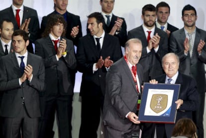 Del Bosque y Blatter muestran, entre los aplausos de los campeones en Sudáfrica, el escudo que España lucirá los próximos cuatro años.