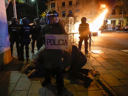 La policía detiene a una persona en Madrid al final de la protesta, mientras al fondo arde el mobiliario urbano.