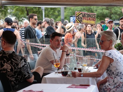 Varios turistas sentados en la terraza de un bar ante el paso de la manifestación organizada por entidades ecologistas, vecinales y sociales, en Barcelona, para reclamar "poner límites" al turismo en la ciudad.