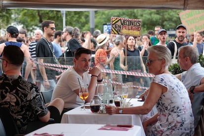 Varios turistas sentados en la terraza de un bar ante el paso de la manifestación organizada por entidades ecologistas, vecinales y sociales, el pasado 6 de julio en Barcelona, para reclamar "poner límites" al turismo en la ciudad.