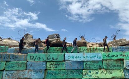 Varios palestinos caminan sobre bloques de hormigón con pintadas políticas, en el puerto marítimo de la ciudad de Gaza.