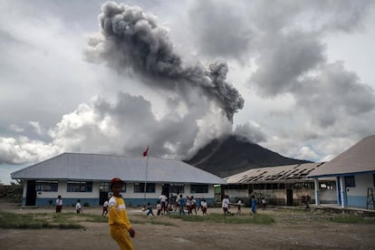 Un grupo de niños juega en una escuela mientras el volcán Monte Sinabung desprende humo, en Karo (Indonesia).
