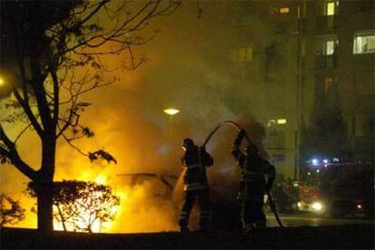 Los bomberos tratan de apagar el fuego que quema un coche en Venissieux, cerca de Lyón, anoche.
