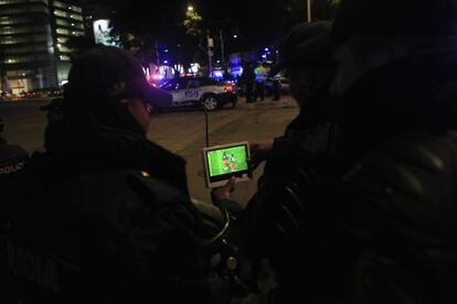 Dos policías mexicanos siguen el partido de su selección en la calle a través de una televisión portátil.