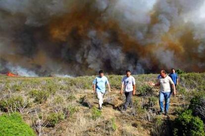 Un grupo de vecinos de la zona arrasada por las llamas se aleja del fuego. El intenso humo da idea de la zona afectada por este incendio que, una vez más, tiene como responsable a la imprudencia humana.