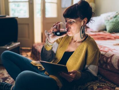 Una chica bebe una copa de vino mientras usa la tableta. GETTY