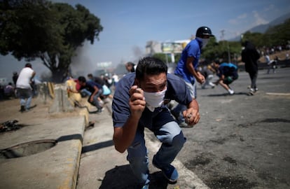 Un manifestante se agacha, sosteniendo unas piedras, durante las protestas en Venezuela.
