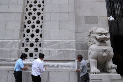 Tres trabajadores envuelven con un film de plástico el edificio del Banco de China para protegerlo del vandalismo, en Hong Kong (China).