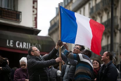 Tres personas colocan una bandera francesa ante el bar le Carillon de París como homenaje a las víctimas del 13-N. | <a href=http://internacional.elpais.com/internacional/2015/11/20/actualidad/1448021198_104861.html target=”blank”>IR A LA NOTICIA</a>