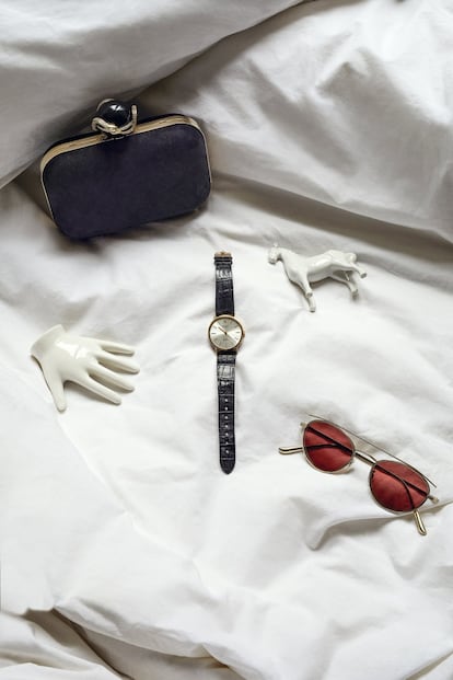 Cartera de ante negro con cierre en forma de serpiente de Jimmy Choo; reloj modelo Cellini con bisel dorado, de Rolex, y gafas de sol de montura metálica y cristales rosados de Oliver Peoples.