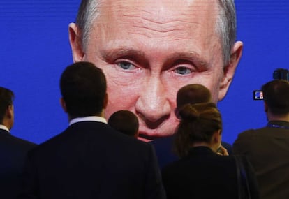 Participantes del Foro Económico Internacional de San Pertersburgo reunidos frente a una pantalla electrónica que muestra al presidente ruso, Vladimir Putin, interviniendo en la sesión.