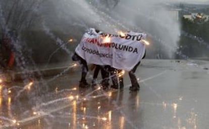 Unos manifestantes se protegen del agua que lanza la policía y los fuegos artificiales de sus compañeros.