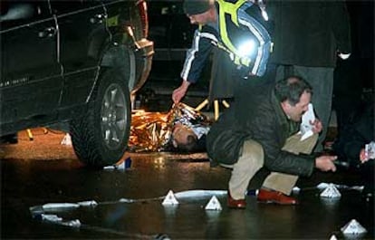 Un policia, al fondo, examina el cadáver de una de las víctimas. Otro agente busca casquillos con una linterna bajo los coches.