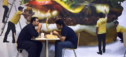 Dos hombres comen hamburguesas en un restaurante de Pakistán.