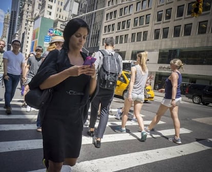 Una mujer mira el m&oacute;vil mientras cruza la Quinta avenida de Nueva York.