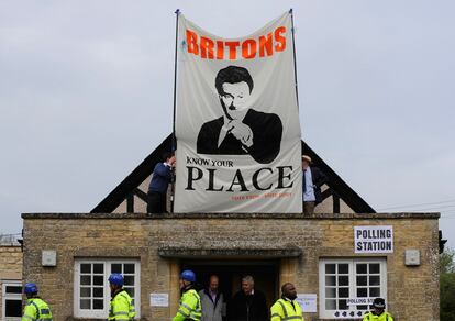 Policías esperan para retirar una pancarta en contra de Cameron en un colegio electoral de Oxfordshire. El incidente ha retrasado dos horas la votación del líder conservador.