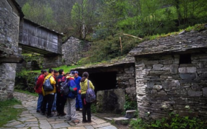 Un grupo de excursionistas observa la arquitectura de pizarra de la aldea de Os Teixois, cerca de la localidad asturiana de Taramundi.