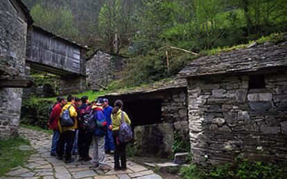 Un grupo de excursionistas observa la arquitectura de pizarra de la aldea de Os Teixois, cerca de la localidad asturiana de Taramundi.