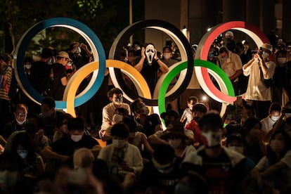 Un grupo de personas espera el inicio de la ceremonia de apertura de los Juegos Olímpicos de Tokio, cerca de la estatua de los Anillos Olímpicos de la capital nipona.