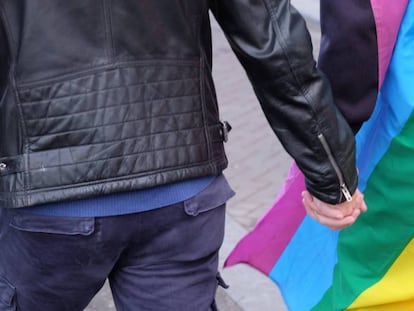 Casal de mãos dadas diante da bandeira multicolorida que identifica a causa LGBTI.