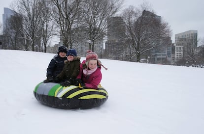 Tres niños se divierten delizándose con un flotador en un parque nevado de Boston.