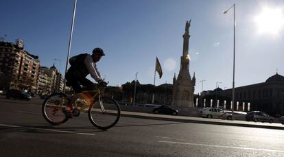 Un ciclista circula frente al monumento a Colón en el Paseo de Recoletos de Madrid.