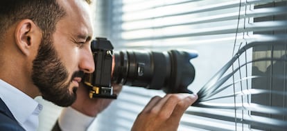 The businessman with a camera photographing through the blinds