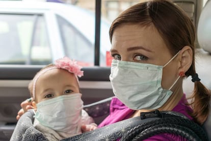 Una madre y su bebé con mascarilla en un coche.