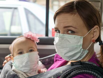 Una madre y su bebé con mascarilla en un coche.