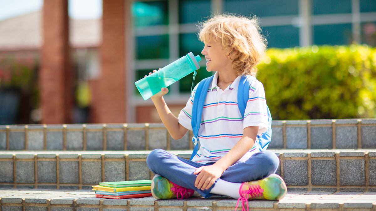 Un niño bebe agua de una botella de plástico durante un día al aire libre.