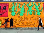 NEW YORK - MAY 02:  People walk by a re-creation of an untitled mural painted by artist Keith Haring on the corner of Houston Street and Bowery in Manhattan May 2, 2008 in New York City. Marking the 50th anniversary of Haring's birth on May 4, a team of artists recreated the mural which was originally done in 1982 as Haring's first major outdoor project. The original mural only existed for a few months before the Day-Glo colors began to decompose in the sun and Haring painted over the piece.  (Photo by Mario Tama/Getty Images)