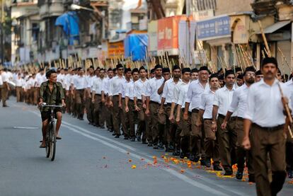 Un hombre monta en una bicicleta al lado de voluntarios de la organización nacionalista hindú Rashtriya Swayamsevak Sangh (RSS), que participan en una marcha previa al festival Dussehra, en Bombay (India).