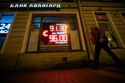 Un hombre camina junto a un panel con información sobre la divisa rusa.