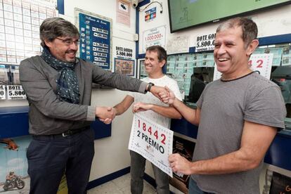 Un responsable de Loteria y Apuestas del Estado, en Las Palmas de Gran Canaria, hace entrega al titular de administración de lotería número 21 de la capital, Juan Miguel Ortega y su hermano José Alberto, del cartel que acredita que parte del segundo premio del sorteo extraordinario de El Niño, celebrado este sábado, ha sido vendido en esta administración.