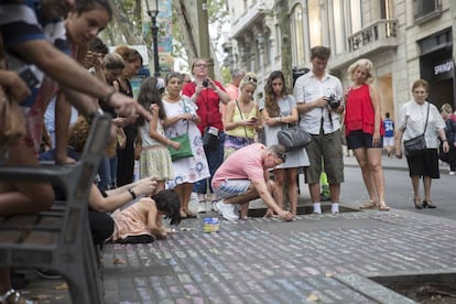 Un grupo de jovenes escriben mensajes de condolencias en el suelo de Las Ramblas.