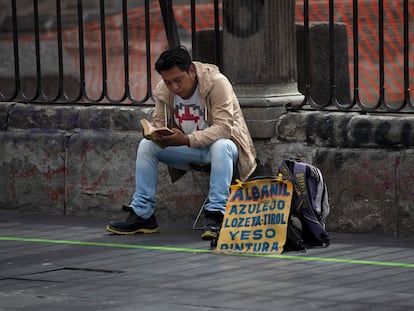 Un hombre lee mientras ofrece servicios de albañilería, frente a la Catedral Metropolitana en Ciudad de México, en agosto de 2020.