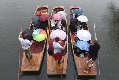 Un grupo de jóvenes se refugia debajo de las sombrillas mientras vanegan por el río Cam en la ciudad universitaria de Cambridge (Inglaterra). Fuertes lluvias y tormentas eléctricas azotaron partes de Gran Bretaña este miércoles.