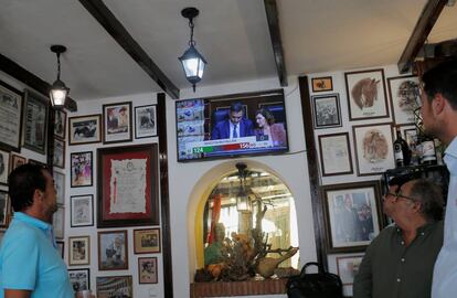 La gente ve a Pedro Sánchez y Carmen Calvo, en una pantalla de televisión durante el debate de investidura en el Parlamento, en un bar en Ronda. 