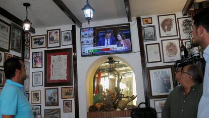 La gente ve a Pedro Sánchez y Carmen Calvo, en una pantalla de televisión durante el debate de investidura en el Parlamento, en un bar en Ronda. 