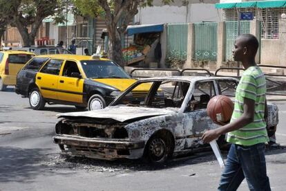 Un joven pasa frente a los restos de un coche quemado ayer durante las manifestaciones en Dakar.