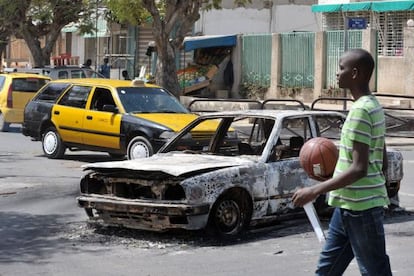 Un joven pasa frente a los restos de un coche quemado ayer durante las manifestaciones en Dakar.