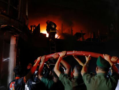 voluntarios sujetan una tubería mientras los bomberos rocían agua para apagar el incendio en un edificio de varios pisos en Dacca, Bangladés, este jueves.