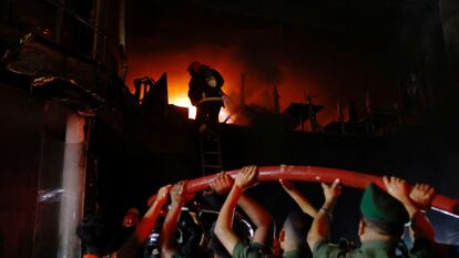 voluntarios sujetan una tubería mientras los bomberos rocían agua para apagar el incendio en un edificio de varios pisos en Dacca, Bangladés, este jueves.