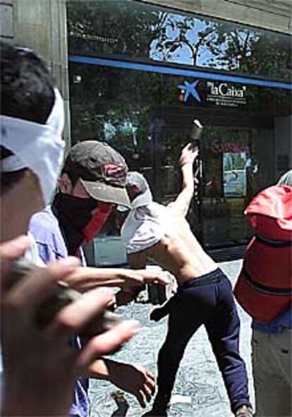 Un grupo de jóvenes lanzan piedras contra una sucursal bancaria en Barcelona durante las protestas antiglobalización.