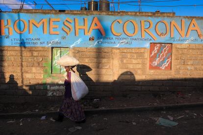 Una mujer con mascarilla camina frente a un eslogan pintado en la pared en idioma suajili que dice: 'Komesha Corona' ('Stop Corona'). El de Mathare es uno de los barrios más pobres de Nairobi (Kenia). Según algunas estimaciones, un millón de personas reside en esta zona.