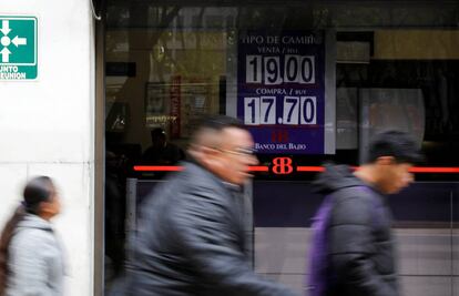 Tres personas pasan por delante de un banco que exhibe el tipo de cambio entre el peso y el d&oacute;lar.