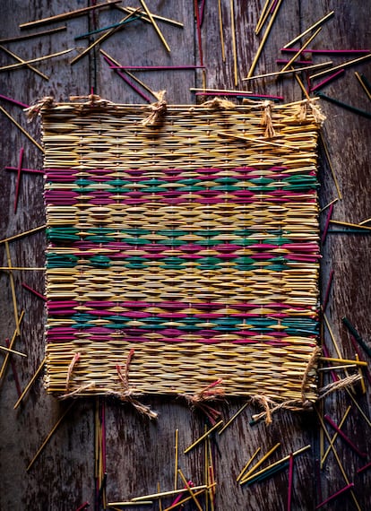 Un 'pedaço', una pieza de junco tejido con colores y diseños tradicionales preparada para ser utilizada como parte lateral de una cesta, junto con los restos de juncos recortados en el telar.
